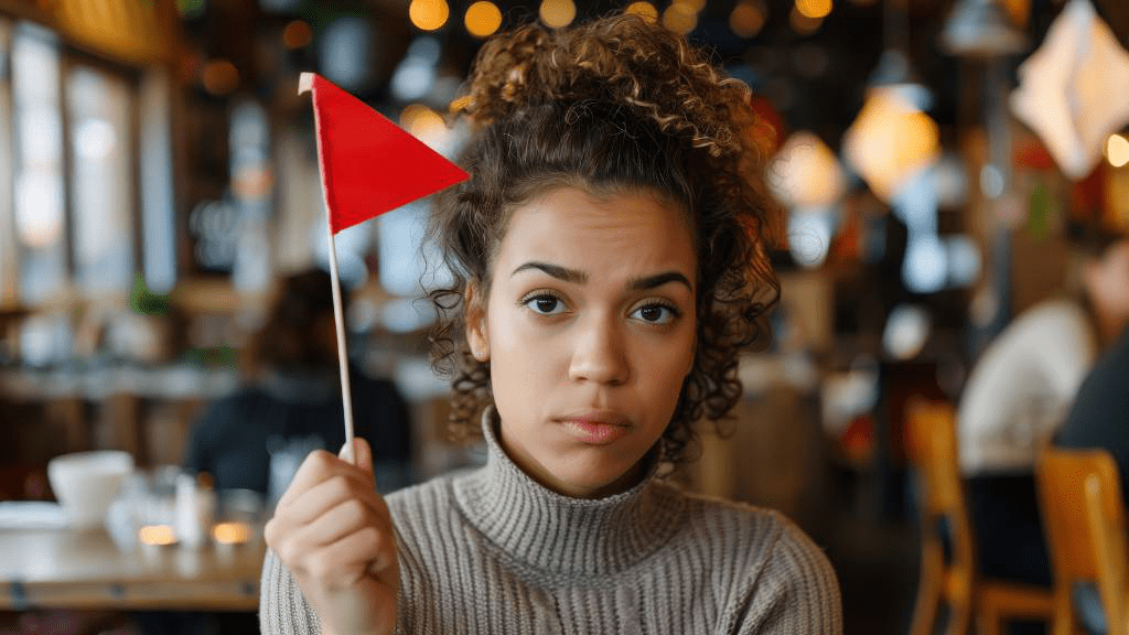 Eine Frau hält eine kleine rote Flagge hoch. Im Hintergrund ist ein Restaurant mit Gästen zu sehen.