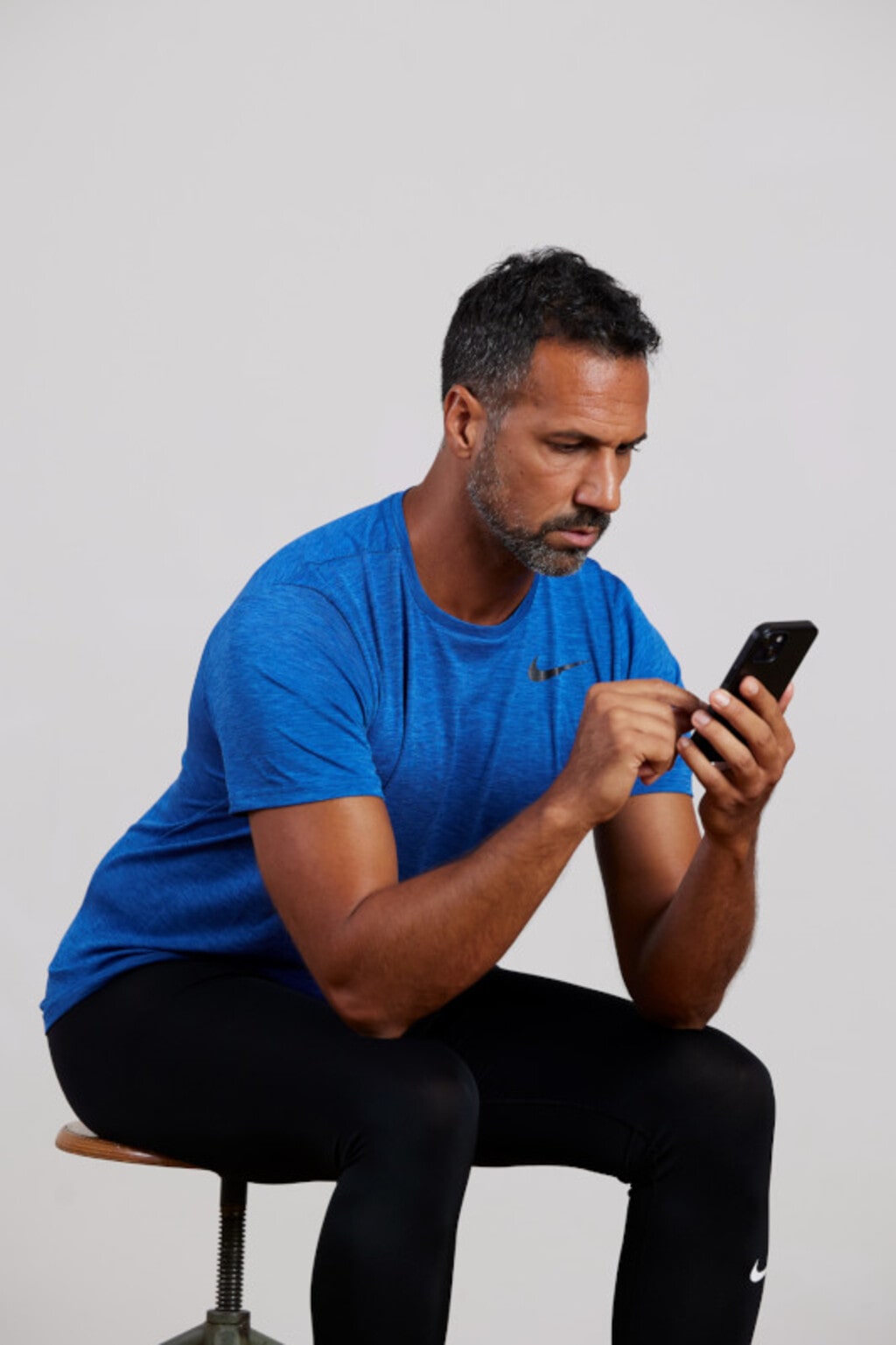 Das Handy im Kutschsitz auf Augenhöhe halten entlastet den Nacken | | © Nils Schwarz Mann schaut ins Smartphone. Er sitzt auf einem Hocker und hat sich mit geradem Rücken nach vorne gebeugt.