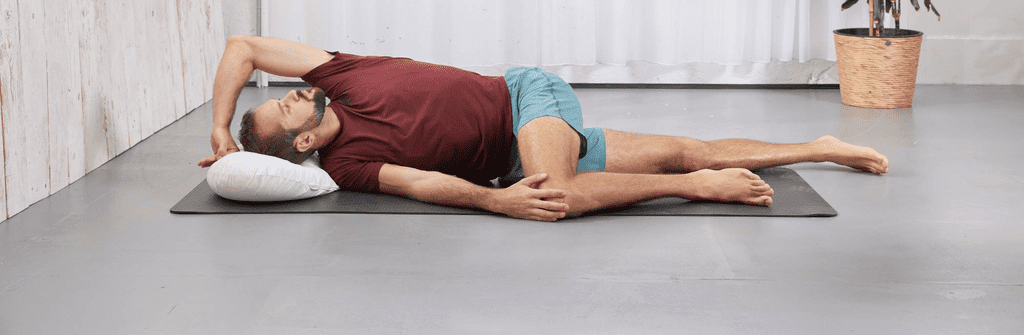 Ein auf dem Boden liegender Mann führt die Drehdehnlagerung, eine Maßnahme gegen Rückenschmerzen durch.