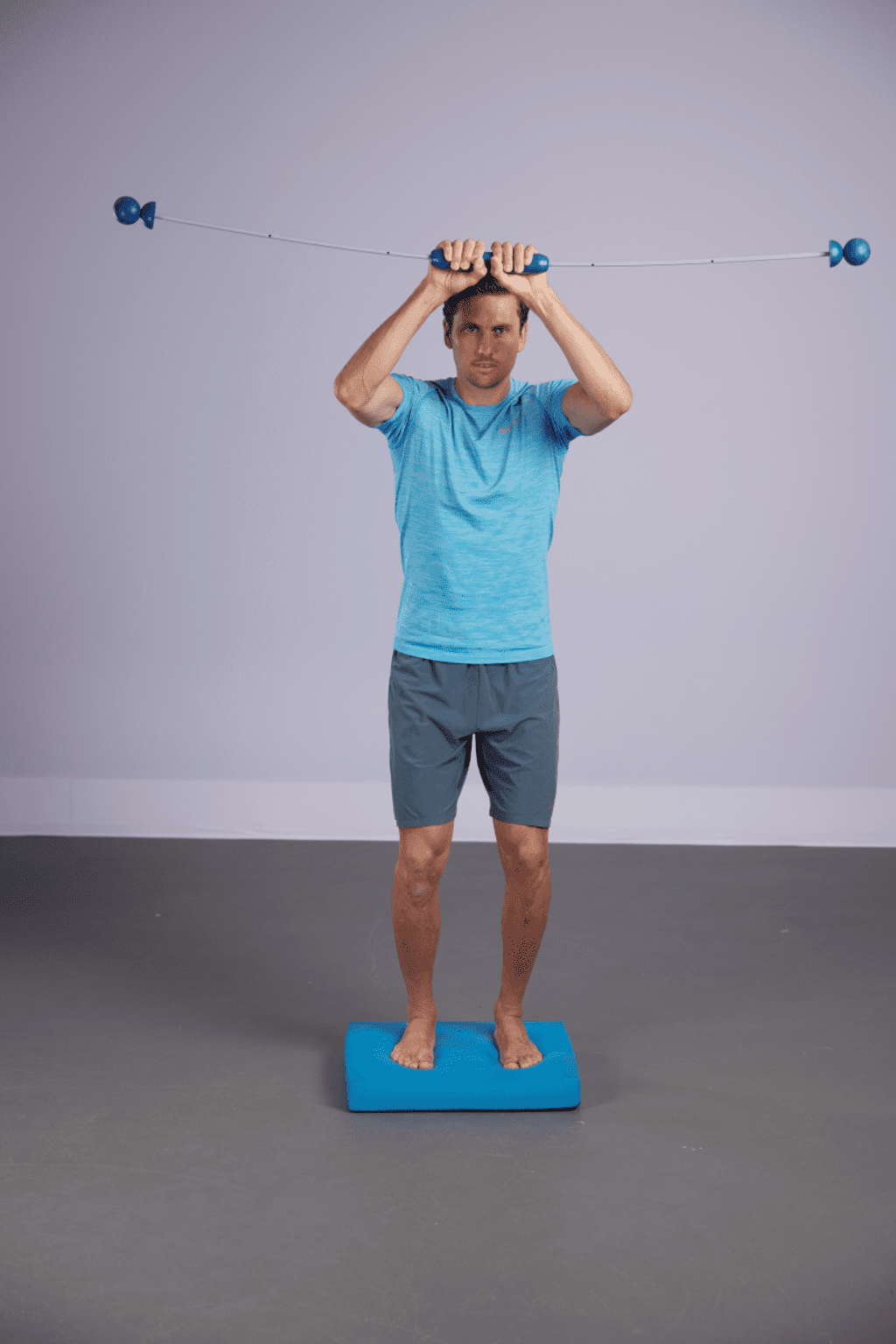 Dreidimensionales Stabilitätstraining auf flexibler Unterlage mit Bewegungsreiz durch Schwingstab. | © Nils Schwarz Ein Mann steht auf einem Bodenkissen und hält einen Schwingstab über den Kopf.