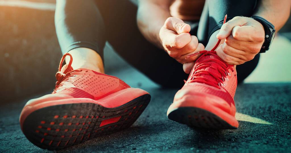 Person in schwarzen Sporttights sitzt auf dem Boden und bindet rote Sportschuhe.