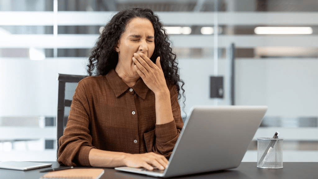 Müde Frau gähnt an ihrem Laptop im Büro – Symbolbild für anhaltende Müdigkeit und Erschöpfung im Arbeitsalltag.