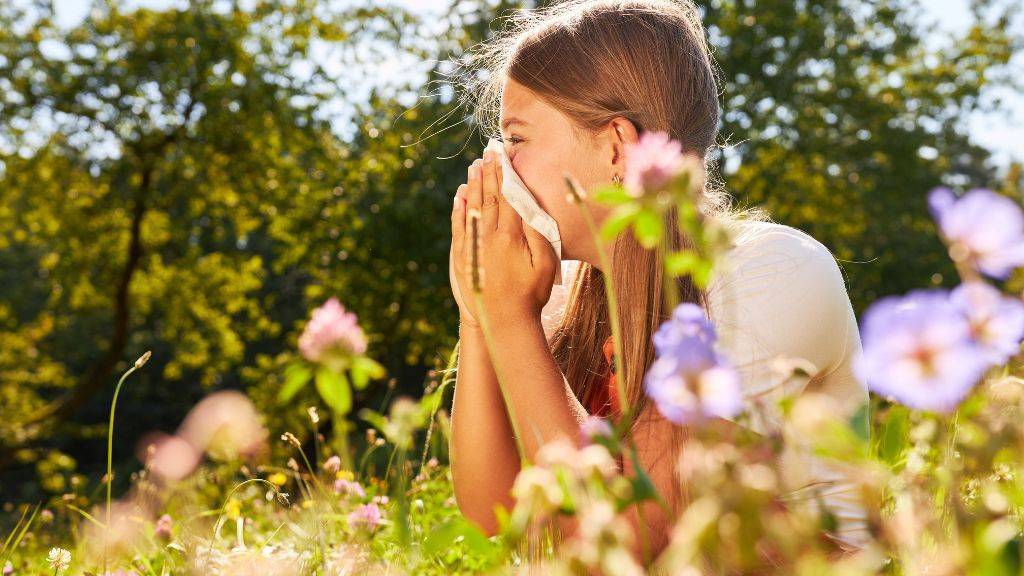 Ein Frau sitzt in einer Wildblumenwiese und putzt sich die Nase.