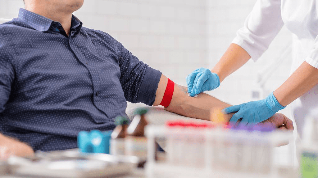 Medizinische Fachkraft in Handschuhen bereitet den Arm eines Blutspenders mit angelegtem Stauschlauch für die Blutentnahme vor.