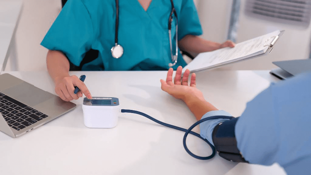 Ärztin misst den Blutdruck eines Patienten mit einem elektronischen Blutdruckmessgerät und bespricht die Ergebnisse.