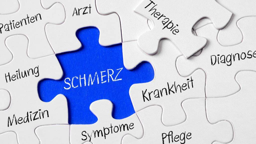 Ein weißes Puzzle auf blauem Grund. Alle Teile sind mit unterschiedlichen Worten beschriftet z. B. Diagnose, Arzt, Heilung. Das Puzzleteil mit der Aufschrift "Therapie" fehlt. An der fehlenden Stelle steht "Schmerz"