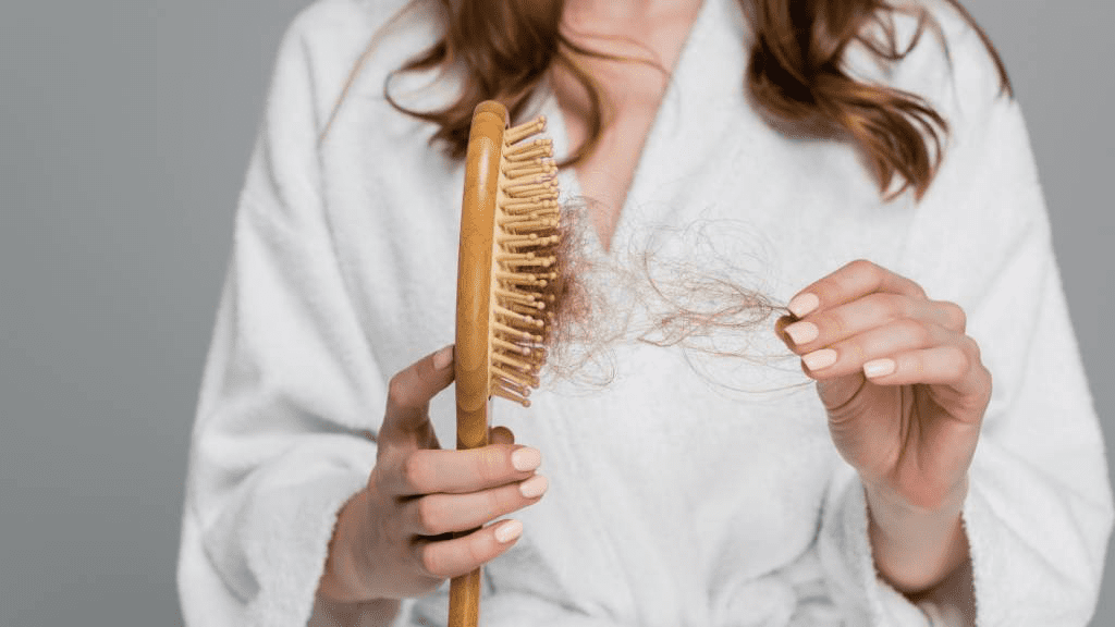 Frau hält Haarbürste mit ausgefallenen Haaren in der Hand – Symbolbild für diffusen Haarausfall, Ursachen wie Stress, Nährstoffmangel oder hormonelle Veränderungen möglich.