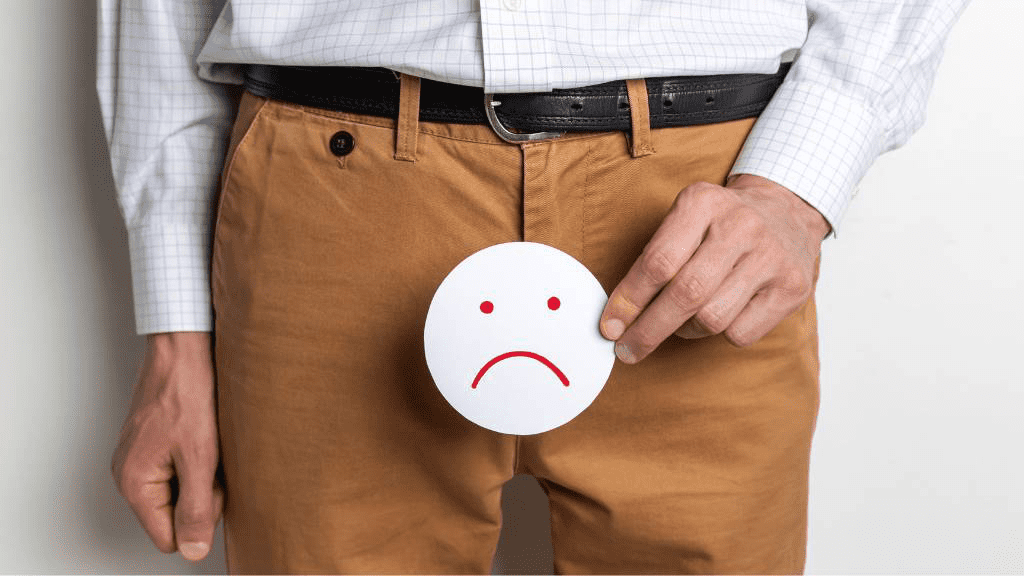 Mann hält ein trauriges Smiley-Schild vor seinen Schritt – Symbolbild für Erektionsstörungen, Potenzprobleme und sexuelle Gesundheit.