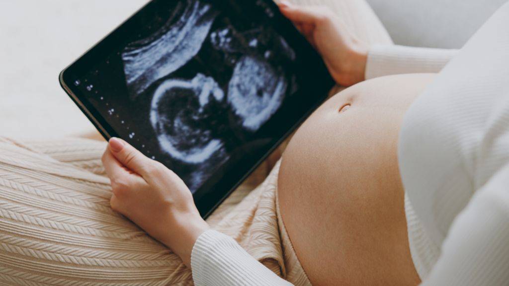 Schwangere mit nacktem Bauch betrachtet Ultraschallbild auf Tablet.