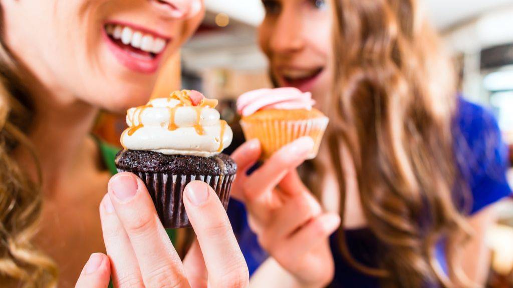 Zwei Frauen essen unterschiedliche Cupcakes.