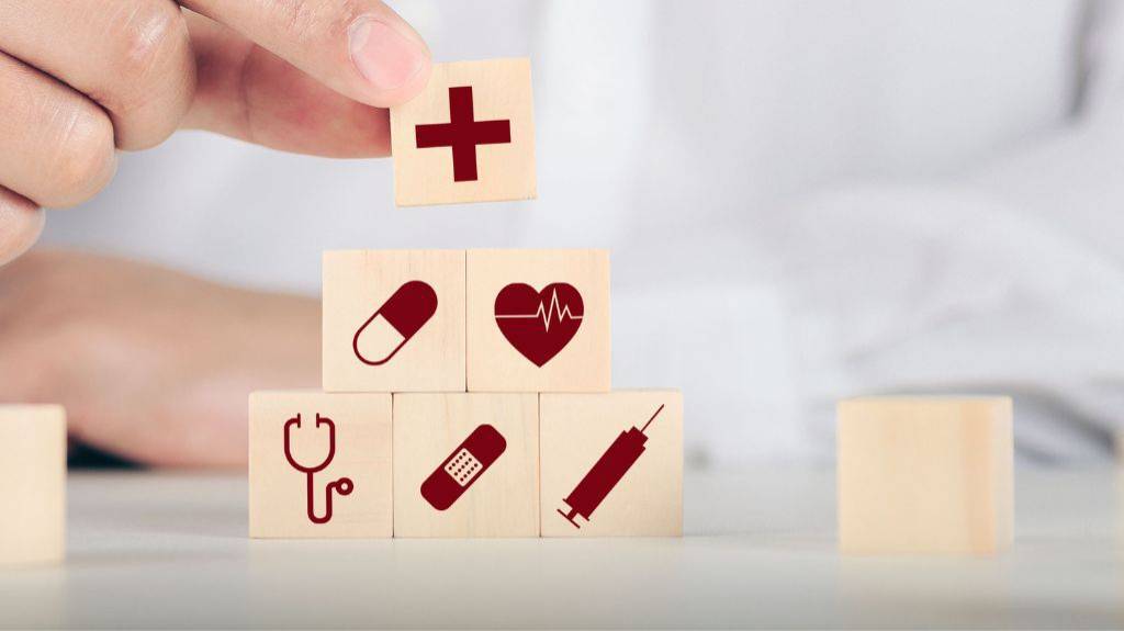Ein Arzt stapelt mehrere Würfel mit Gesundheitssymbolen aufeinander, z. B. Stethoskop, Pflaster, Tablette.