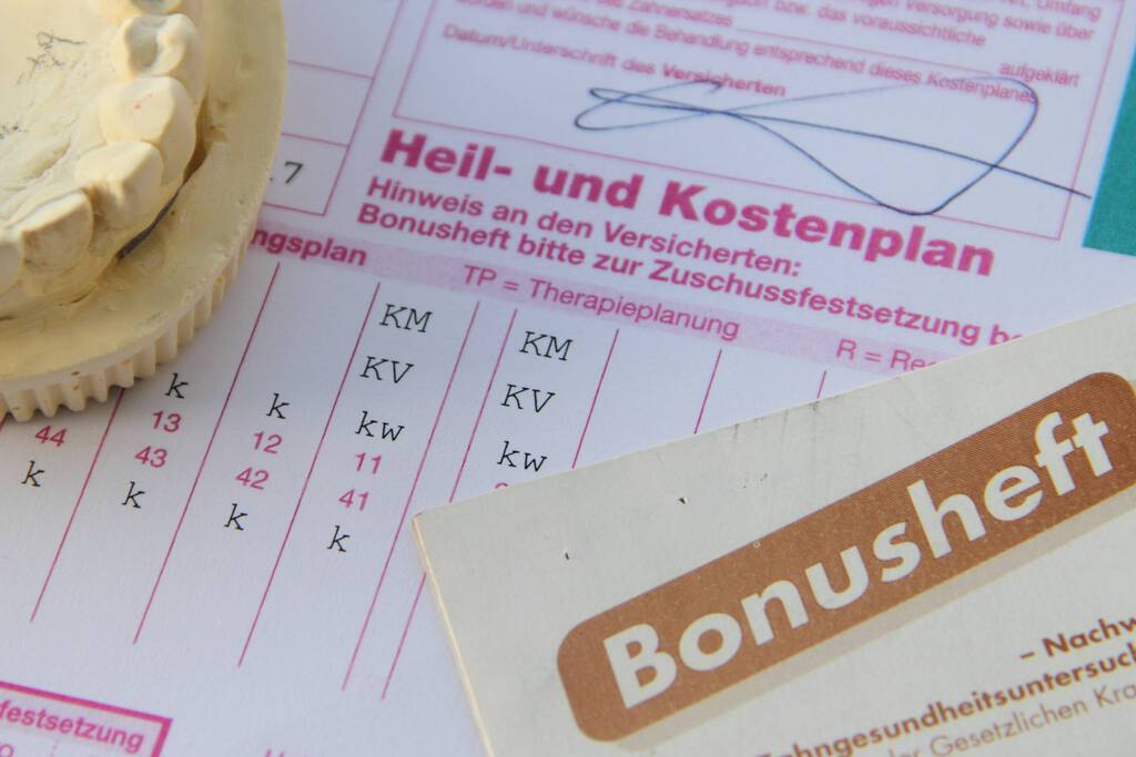 Ein Heil- und Kostenplan, sowie ein Bonusheft als Nachweis der Zahngesundheitsuntersuchungen und Abdrücke von unteren Zahnreihen gesammelt an einer Stelle platziert.