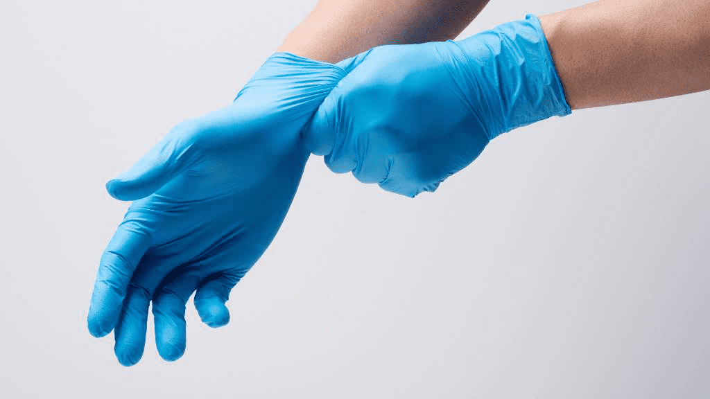 Blaues Paar Einweghandschuhe aus Nitril an Händen, die gerade angezogen werden; Darstellung von hautfreundlicher, sicherer Schutzausrüstung für medizinische oder hygienische Anwendungen.
