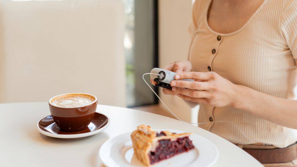 Eine Frau nutzt ihre Insulin-Pumpe, bevor sie einen Milchkaffee und ein Stück Kuchen isst.
