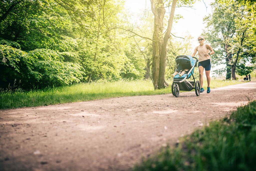 Joggerin mit Laufkinderwagen im Park - ein gutes Hilfsmittel, auch nach der Schwangerschaft aktiv zu sein.