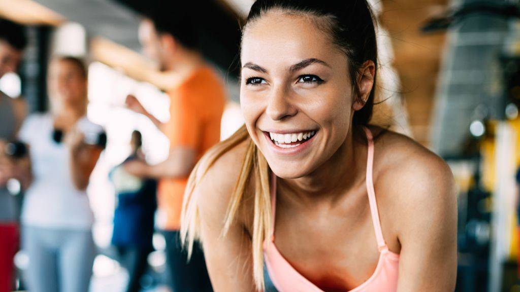 Eine Frau steht gut gelaunt im Fitnessstudio.