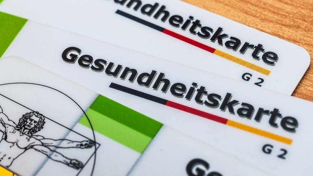 Zwei Gesundheitskarten liegen auf einem Honztisch.