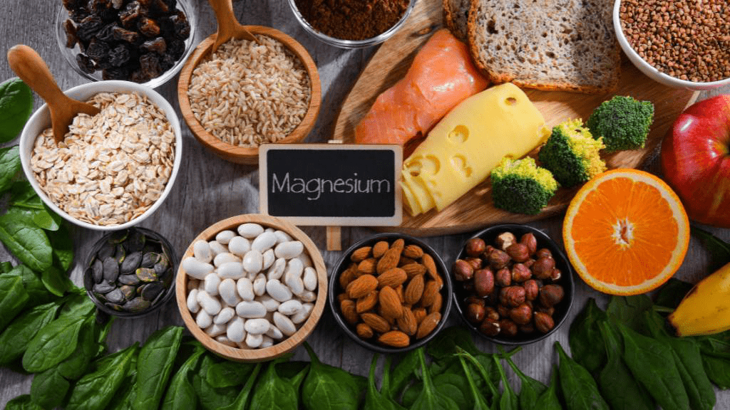 Magnesiumreiche Lebensmittel wie Haferflocken, Nüsse, Bohnen, Lachs, Brokkoli und Vollkornprodukte neben einer Tafel mit Schriftzug Magnesium
