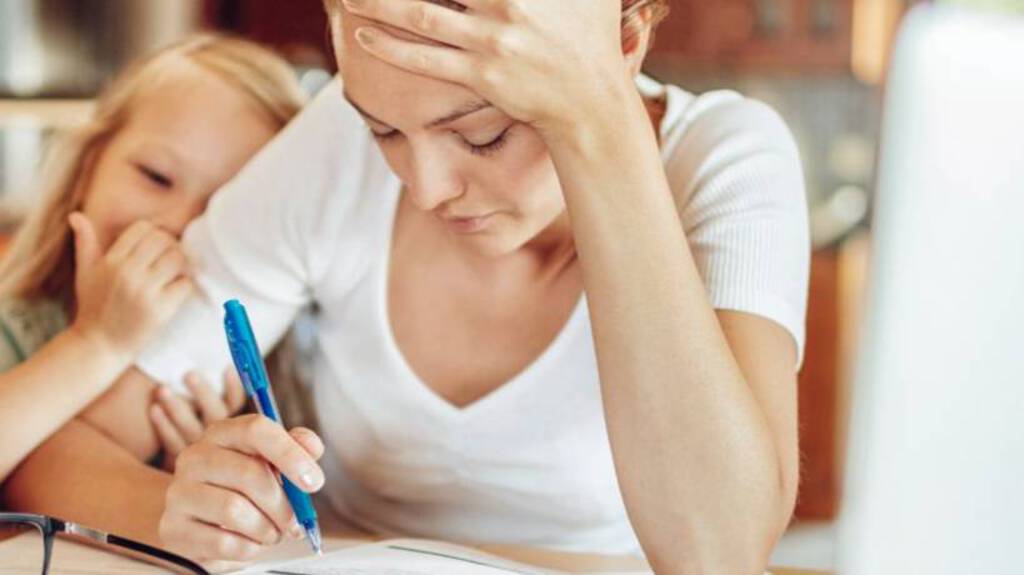 Eine Mutter sitzt am Tisch und arbeitet. Ein Kind sitzt daneben.