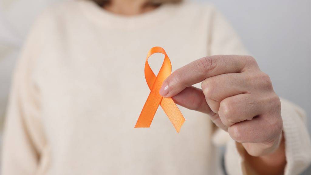 Eine Frau hält die orange Schleife, das Zeichen für Solidarität mit Menschen mit Multipler Sklerose in die Kamera.