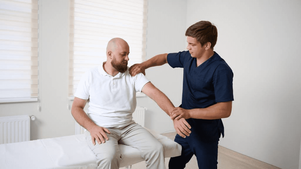 Physiotherapeut untersucht den Arm eines Patienten, der auf einer Behandlungsliege sitzt. Der Therapeut testet Beweglichkeit und Schulterfunktion in einer hellen Praxis.