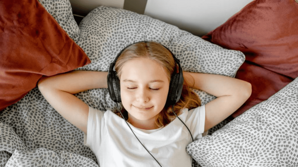 Ein Kind welches entspannt auf einem Bett liegt mit Kopfhörern und lächelt 