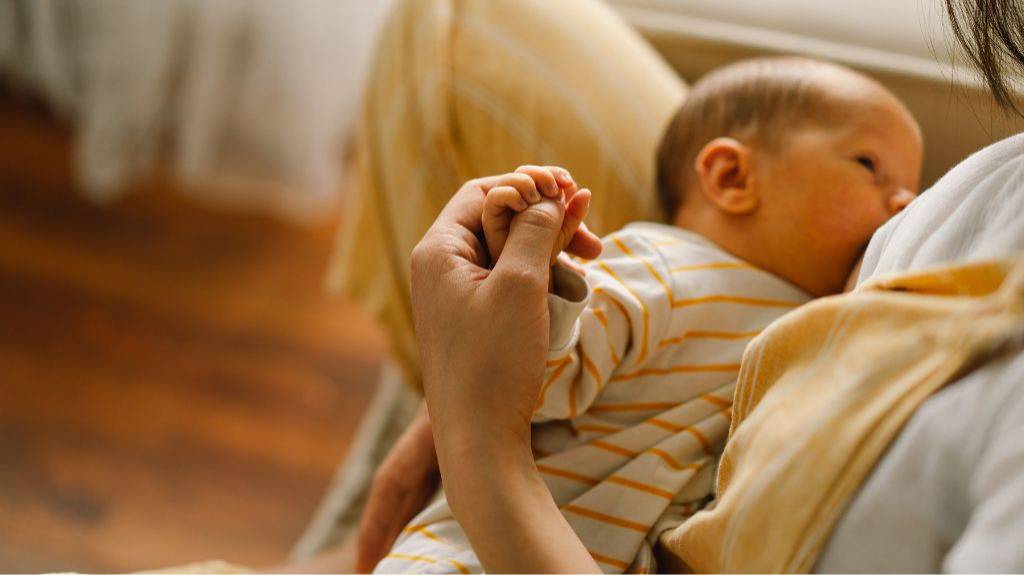 Eine Frau stillt ihr Baby in einem ruhigen Raum. Warme Farben und viele Gelbtöne.