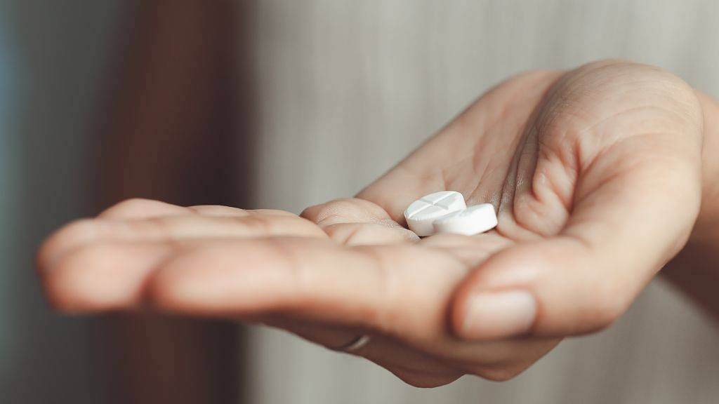 Eine Hand hält zwei runde Tabletten mit einer Kerbe.