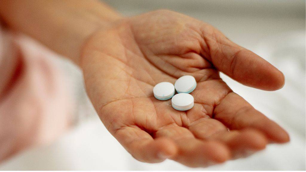 Eine Hand hält drei weiße Tabletten.