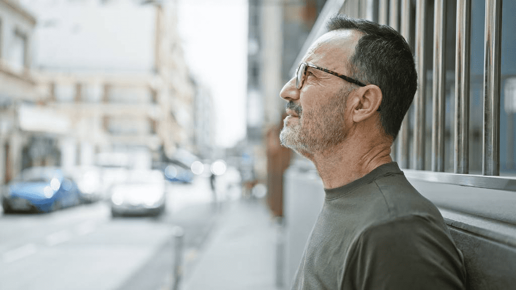 Älterer Mann mit Brille blickt nach oben in einer Stadtstraße – Symbolbild für altersbedingte Sehprobleme und Veränderungen des Sehvermögens im Alltag.