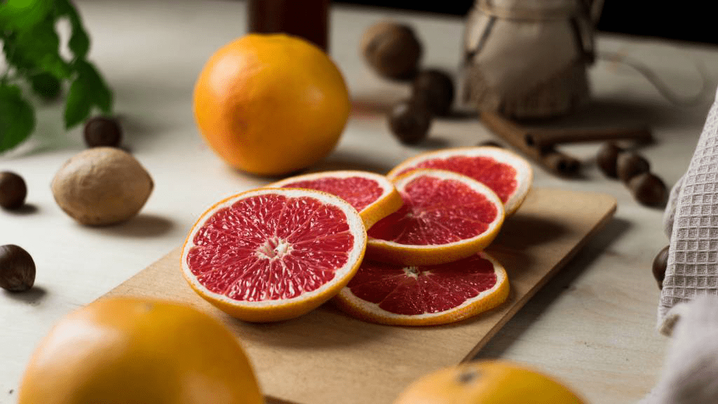 Frisch aufgeschnittene Grapefruit-Scheiben auf einem Holzbrett, umgeben von ganzen Grapefruits, Nüssen und Kräutern – symbolisieren Bitterstoffe und gesunde Ernährung.
