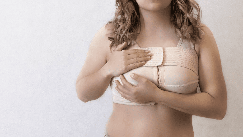 Frau nach Brustoperation mit medizinischem Kompressions-BH und Verband, hält schützend die Brust – Darstellung der Heilungsphase und Nachsorge nach einer Brust-OP